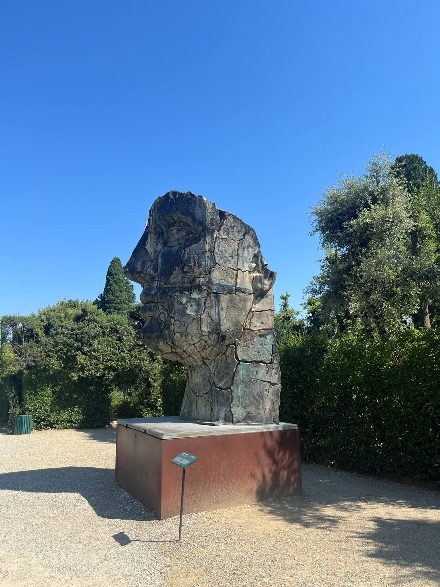 Portrait of Tindaro Screpolato from the front of the Prato dei Castagni, the bronze silhouette rising above trimmed hedges, small info plaque visible at the foot of the plinth