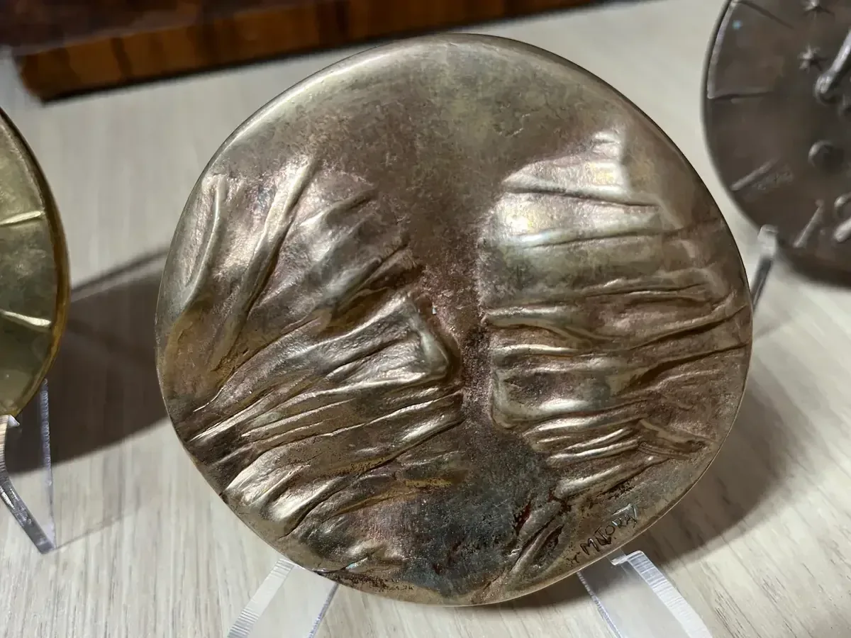 La Conversation — Igor Mitoraj, close-up of worn iridescent obverse with MITORAJ signature, flanked by gilt and dark patina reverses