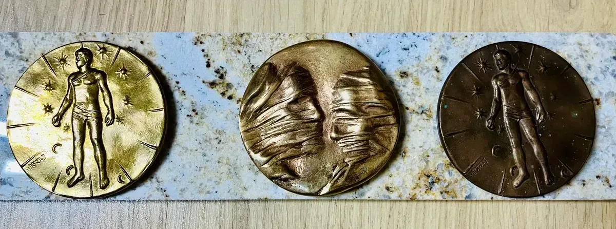 La Conversation — Igor Mitoraj, three specimens on marble slab: gilt, worn gold, and dark brown patinas — obverse and reverse variants
