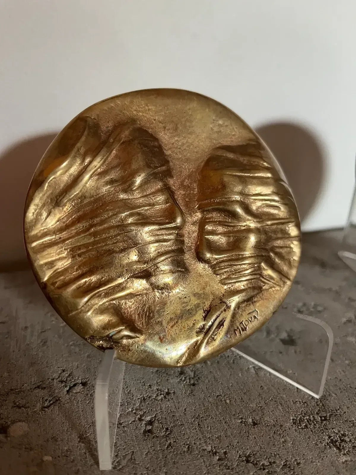 La Conversation — Igor Mitoraj, obverse (two veiled profiles), deep amber-gold patina on acrylic stand, white background