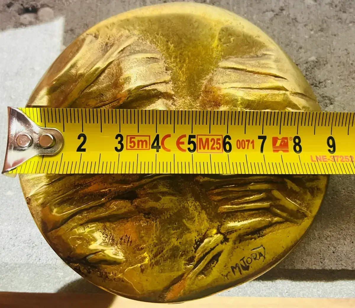 La Conversation — Igor Mitoraj, scale reference: measuring tape showing ~7 cm medal diameter, gilded bronze obverse