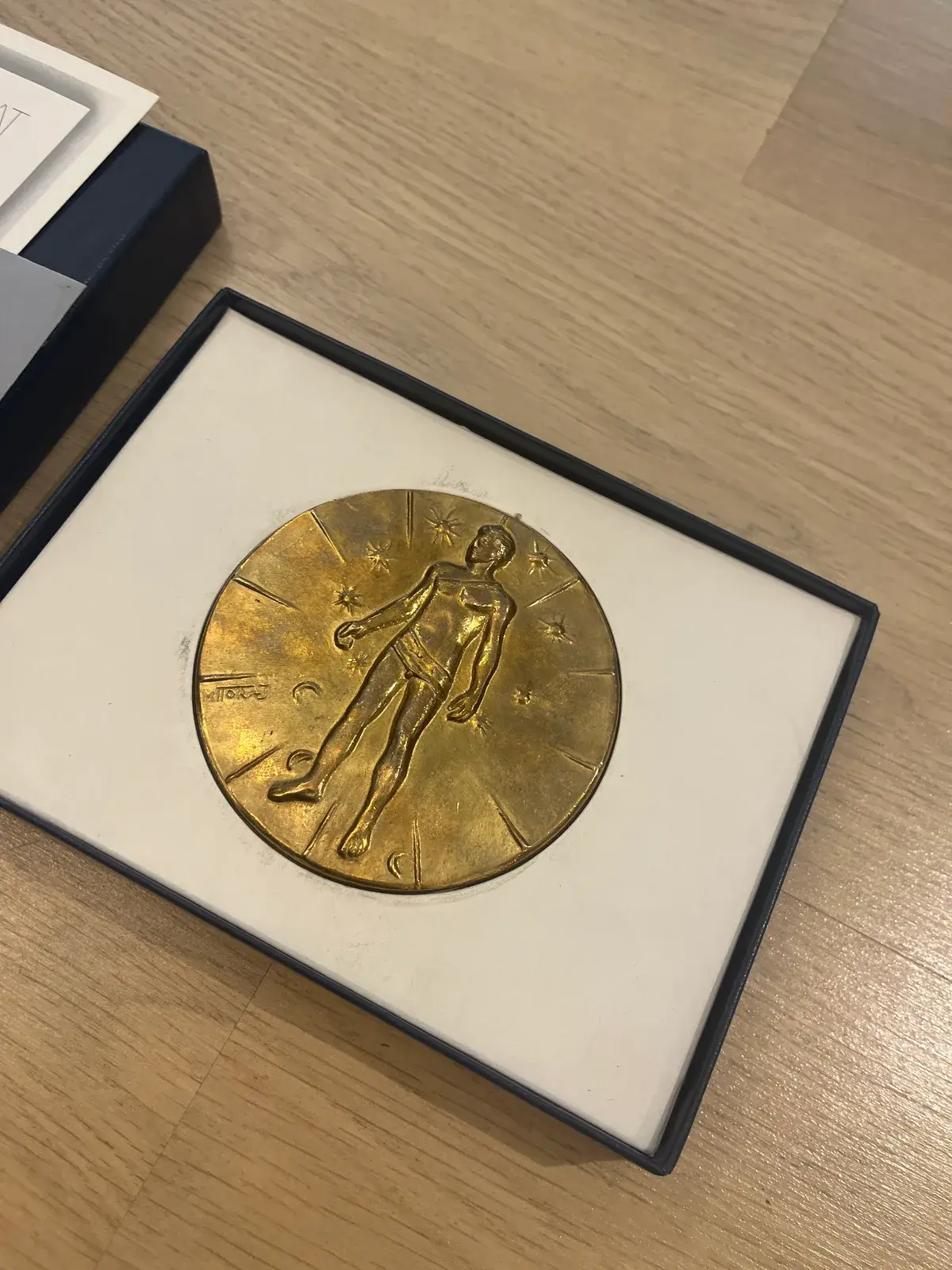 Mitoraj Articulations — gilded bronze medal close-up, standing figure amid stars