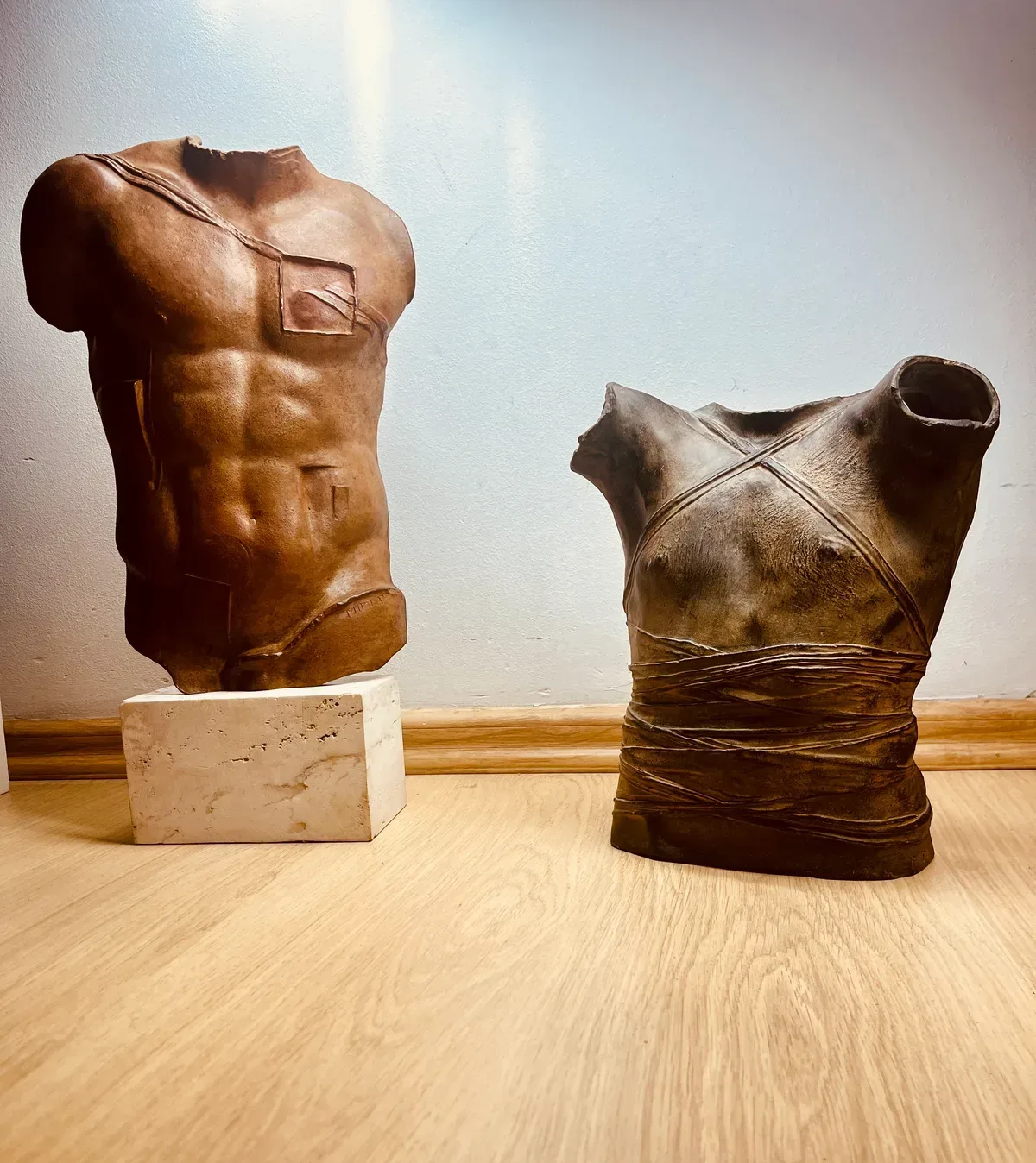 Persée (1988) — Igor Mitoraj, brown patina bronze torso displayed alongside a wrapped bronze torso, two-piece collection grouping, natural daylight, oak floor, private collection Warsaw