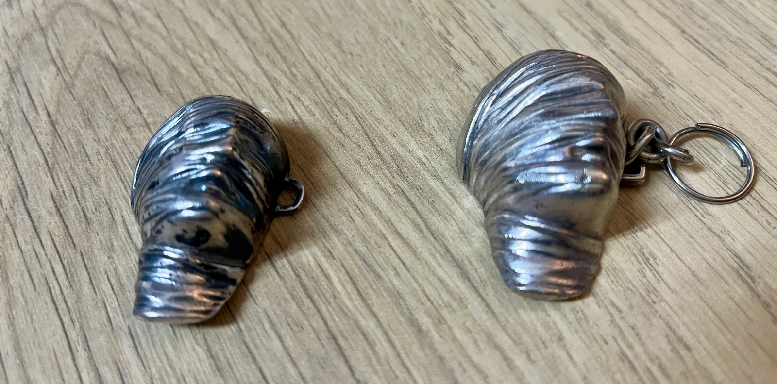Testa Addormentata — pair of Mitoraj Amnesty International silver pendants side by side, three-quarter view on wood