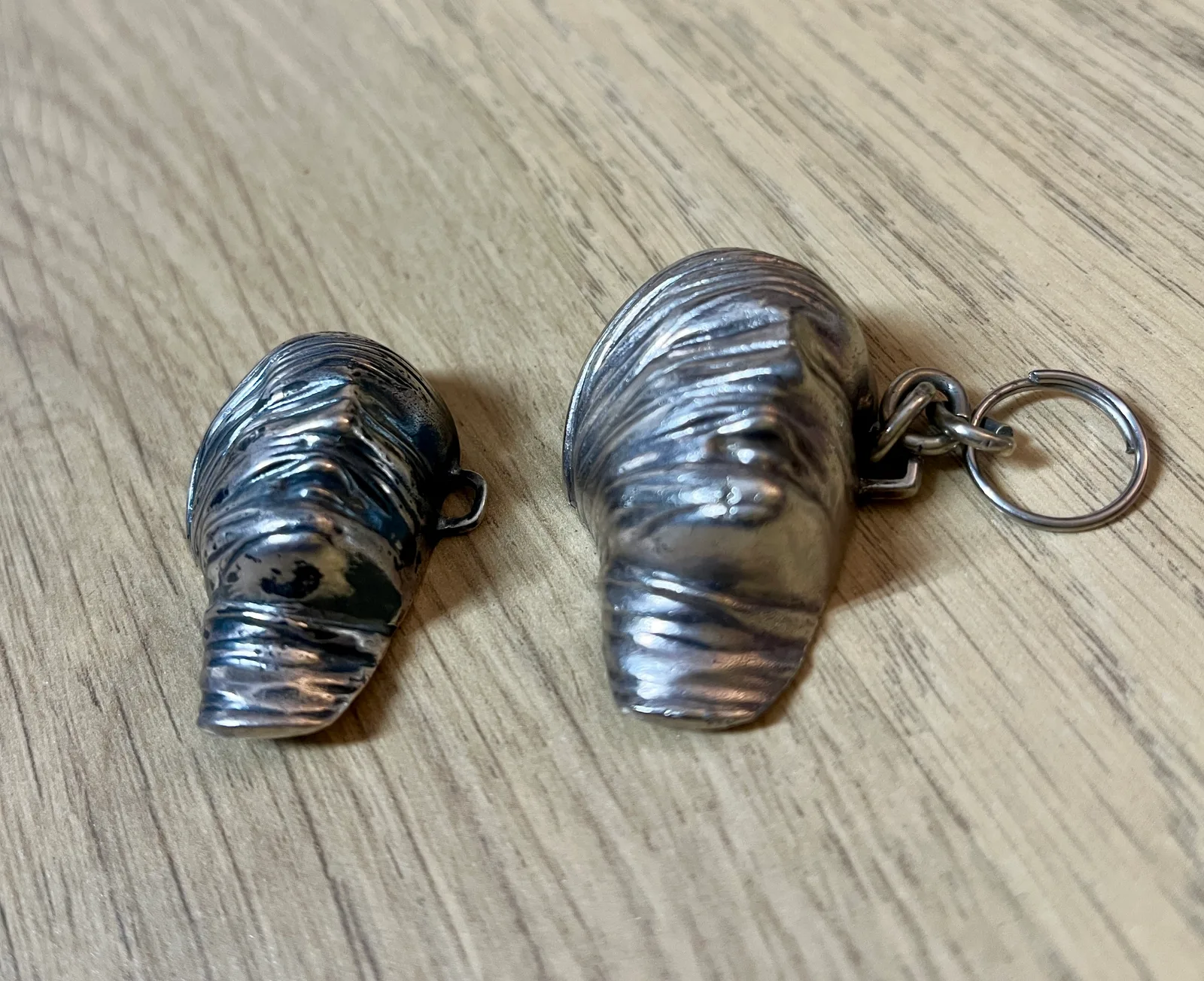 Testa Addormentata — pair of Mitoraj Amnesty International silver pendants, close comparison of bandaged head surface